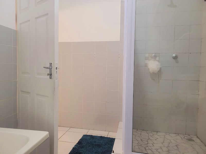 A functional bathroom featuring a tiled shower enclosure and neutral wall tiling, offering a clean canvas for potential modern updates.