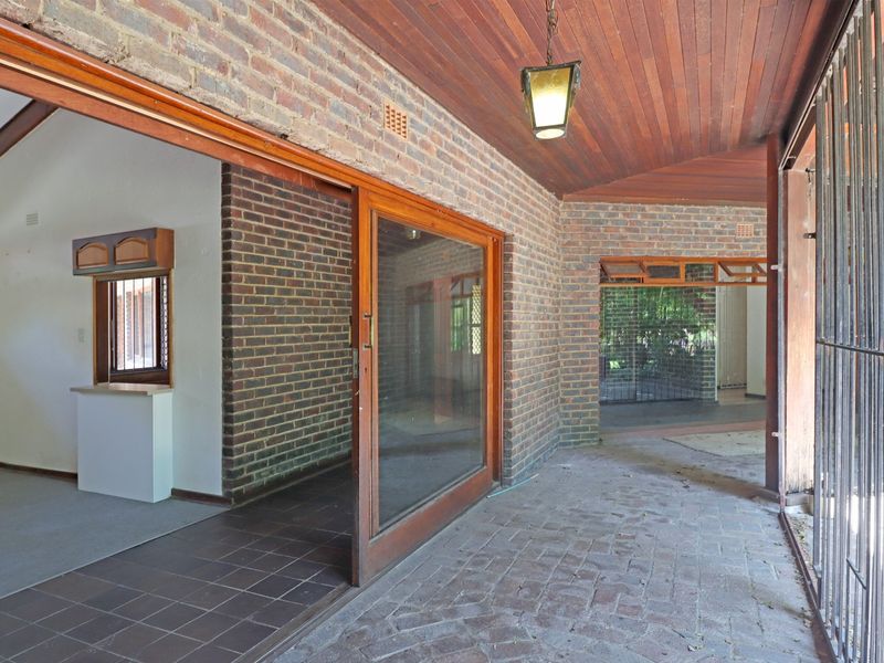 A covered patio area featuring exposed brick walls, timber ceiling, and sliding glass doors leading into the interior living space.