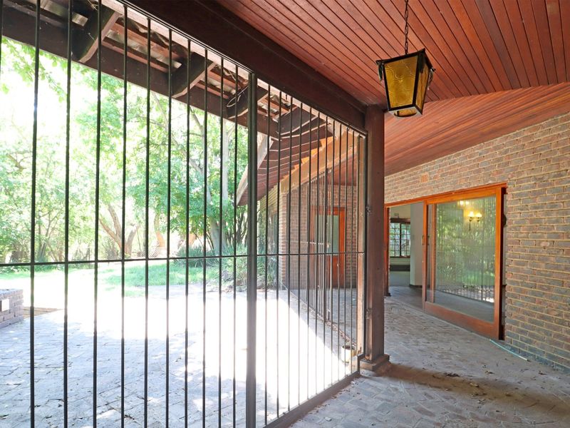A covered outdoor patio featuring exposed brick walls, timber ceiling, and paved flooring, secured with a metal gate and providing access to the interior.