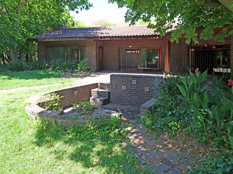 Rear view of a brick house featuring a patio area, brick retaining walls, and established garden landscaping.