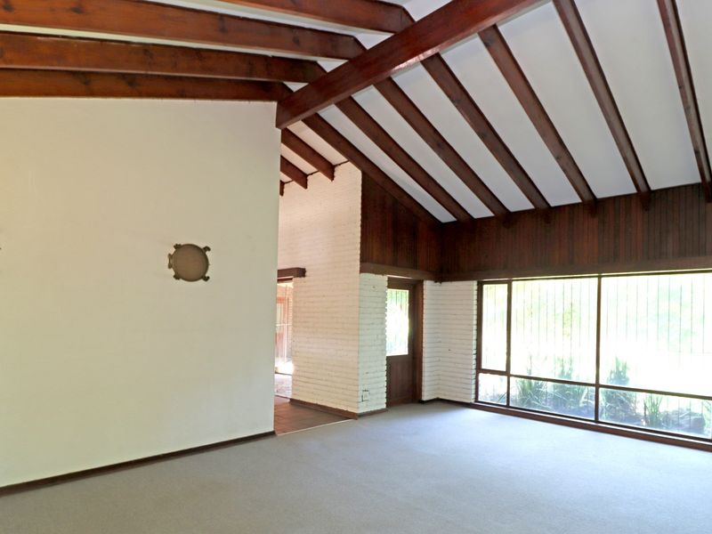 Spacious living area featuring vaulted ceilings with exposed timber beams, painted brick walls, and large windows providing ample natural light.