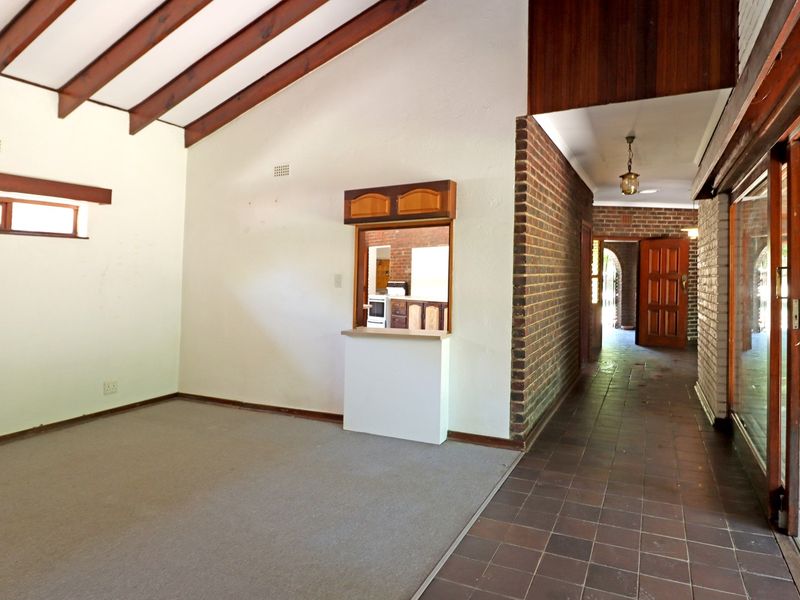 Spacious living area featuring exposed timber beams, a vaulted ceiling, brick accent wall, and a convenient serving hatch connecting to the kitchen area.