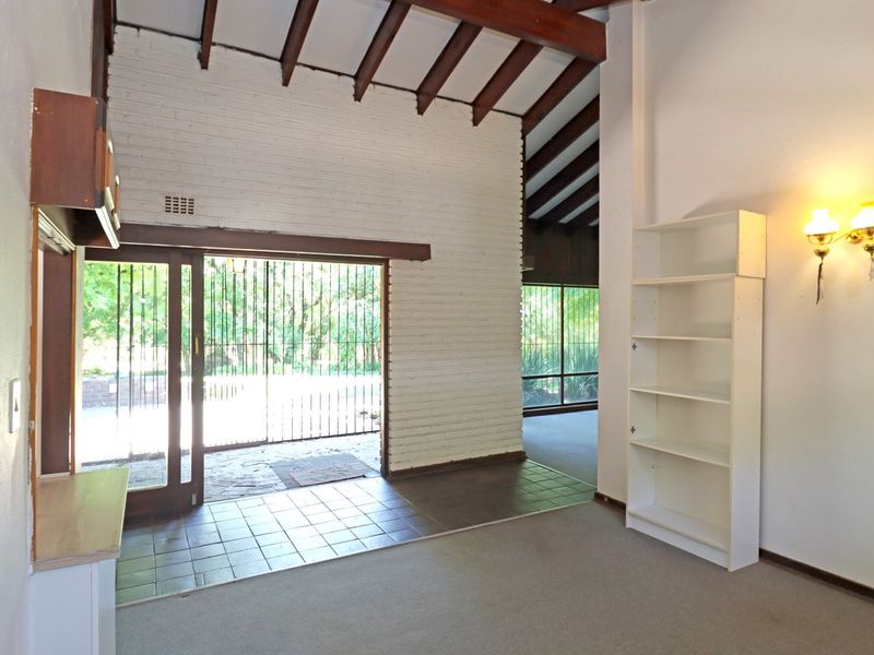 Spacious living area featuring exposed timber beams, a painted brick feature wall, and direct access to the outdoor area through sliding glass doors.