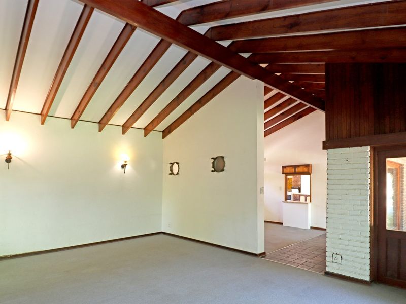 Spacious living area featuring vaulted ceilings with exposed timber beams, a painted brick fireplace surround, and neutral wall finishes.