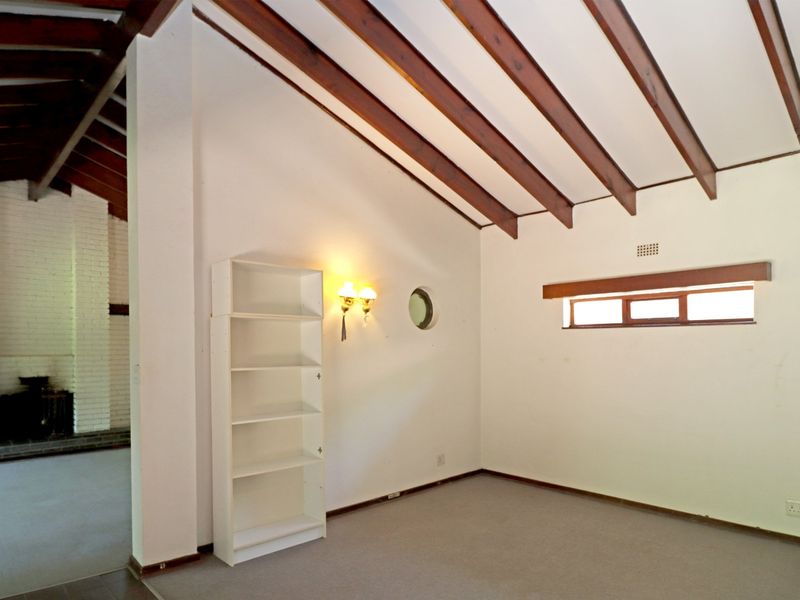Spacious living area featuring a vaulted ceiling with exposed timber beams, a brick fireplace, and unique architectural details including a porthole window.