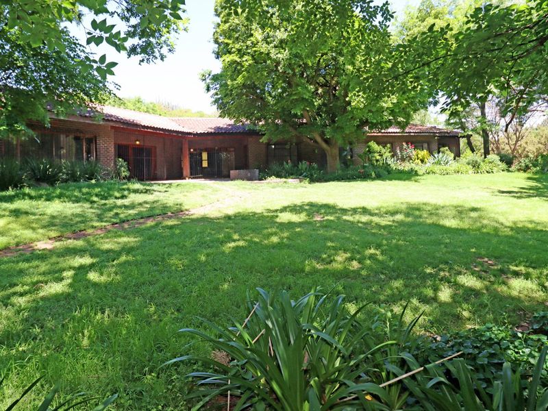 A spacious rear garden featuring a large lawn, mature trees, and a brick-built house with a tiled roof.