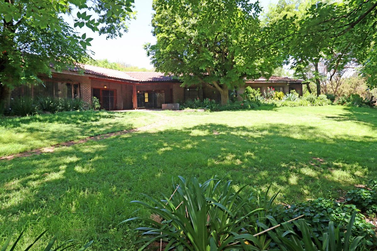 A spacious rear garden featuring a large lawn, mature trees, and a brick-built house with a tiled roof.