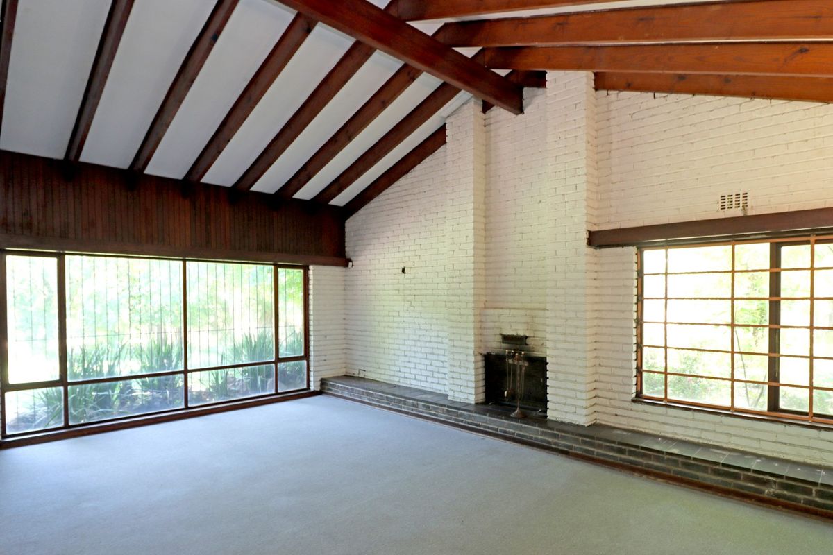 Spacious living room featuring exposed timber ceiling beams, a painted brick fireplace, and large windows providing ample natural light.