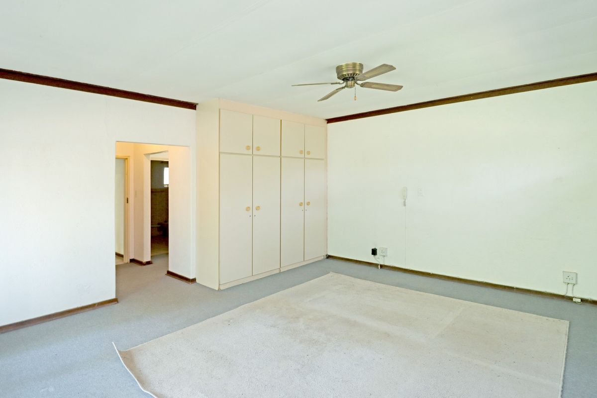 A spacious, empty bedroom featuring built-in cupboards, a ceiling fan, and neutral wall finishes, offering a blank canvas for potential updates.