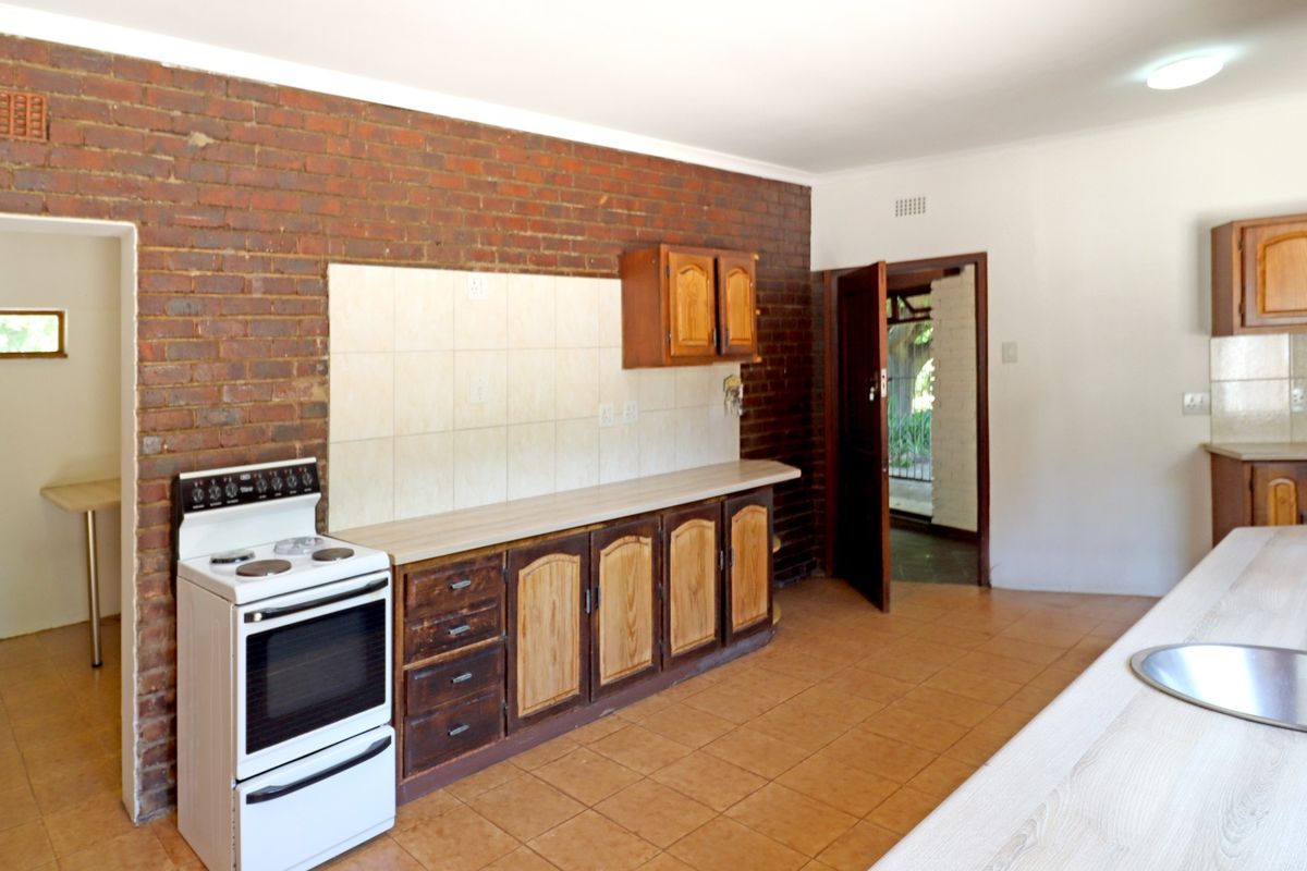 A functional kitchen featuring exposed brick walls, tiled flooring, built-in wooden cabinetry, and a freestanding stove with a tiled splashback.