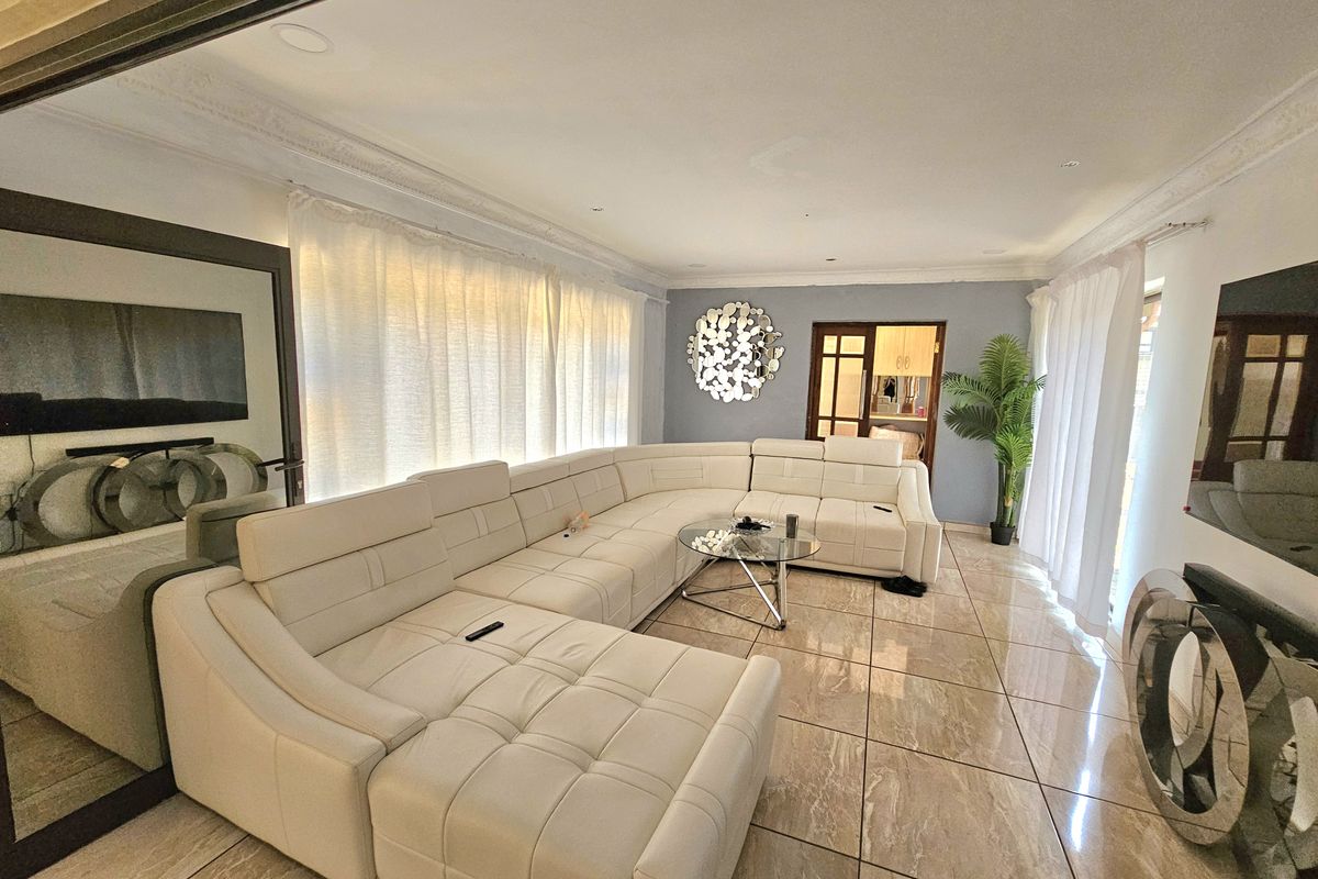 Spacious living room featuring large format polished floor tiles, decorative ceiling cornicing, and recessed lighting, creating a bright and modern atmosphere.