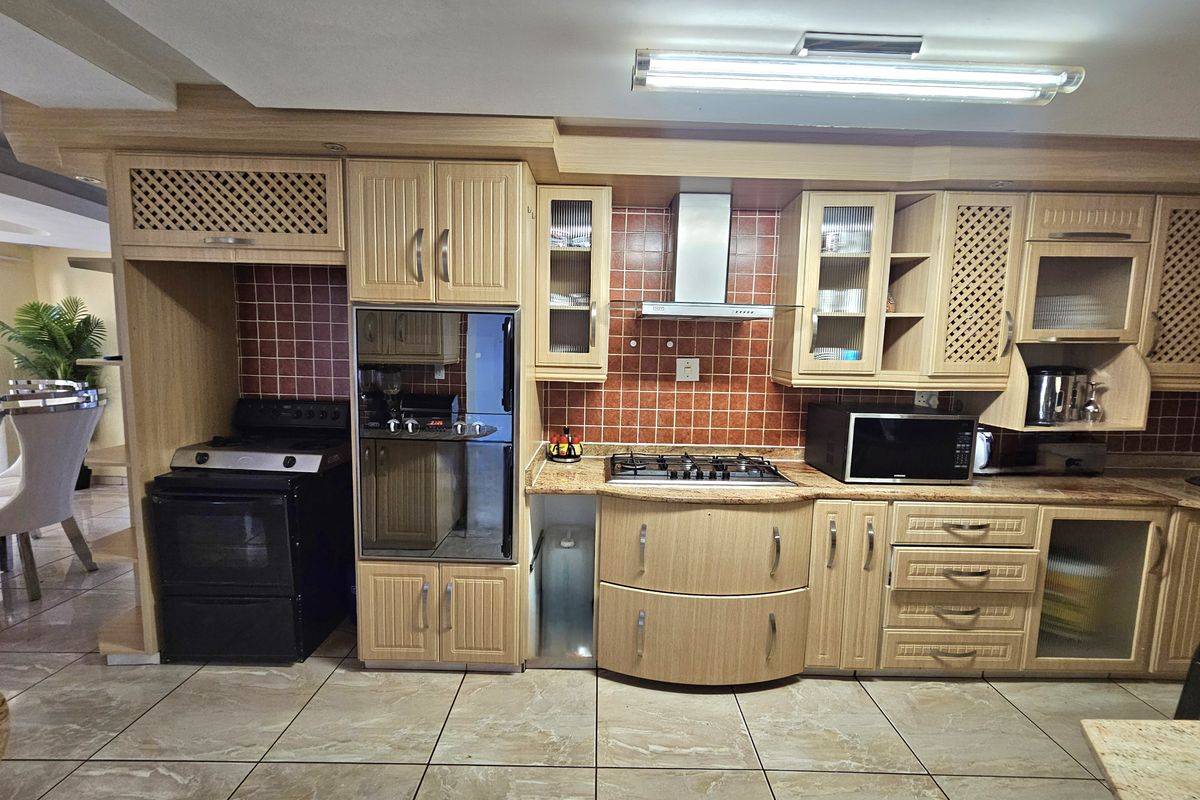 A functional kitchen featuring light wood cabinetry, granite countertops, a gas hob with extractor fan, and a tiled backsplash.