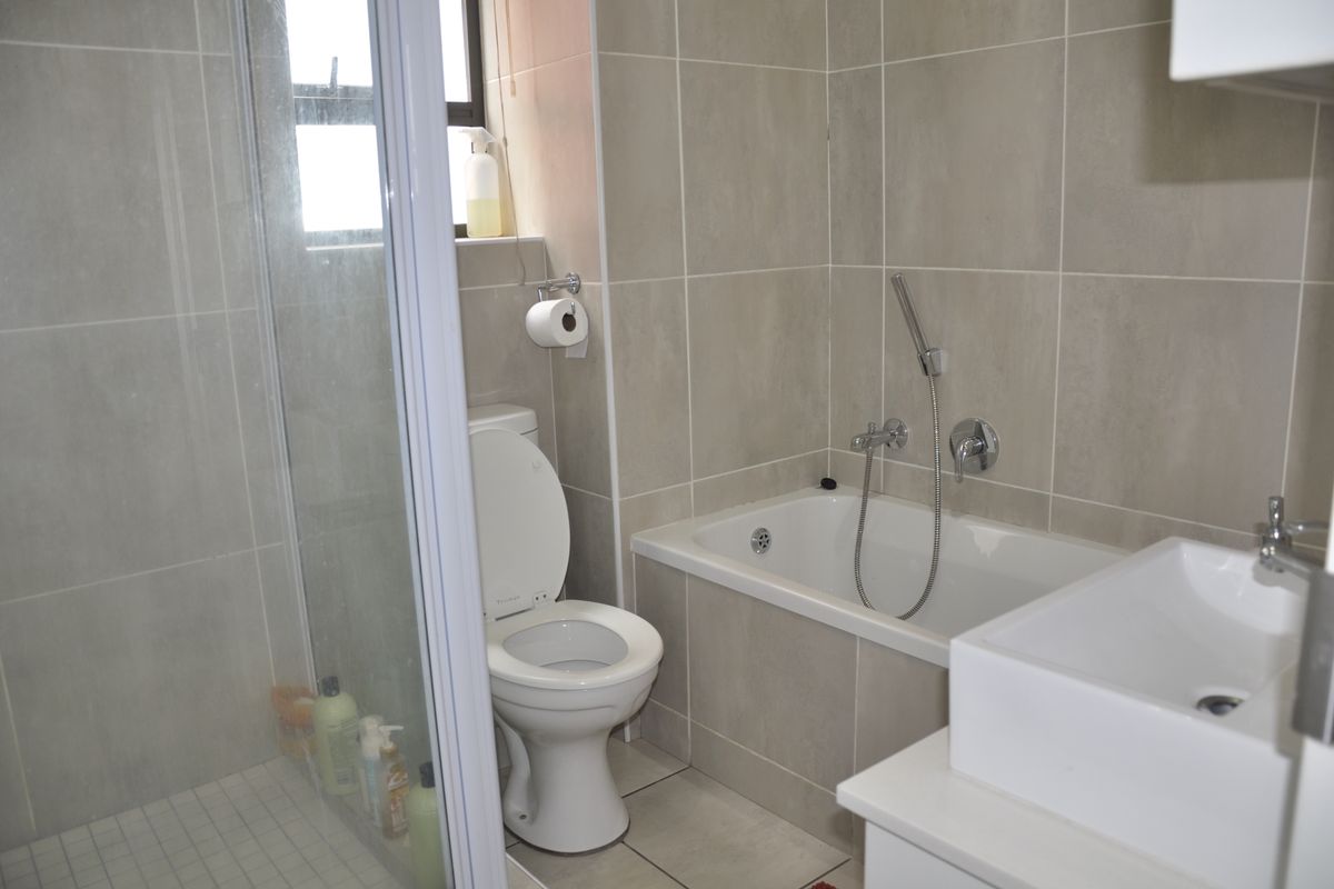 A modern bathroom featuring a glass-enclosed shower, a bathtub with a handheld showerhead, a toilet, and a contemporary basin with neutral wall tiling.