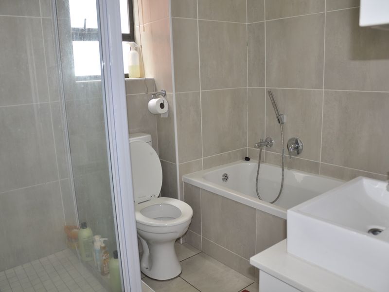 A modern bathroom featuring a glass-enclosed shower, a bathtub with a handheld showerhead, a toilet, and a contemporary basin with neutral wall tiling.