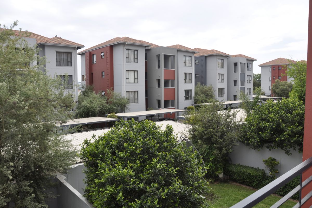 View of the apartment complex exterior featuring multi-story residential blocks, covered parking structures, and landscaped garden areas.