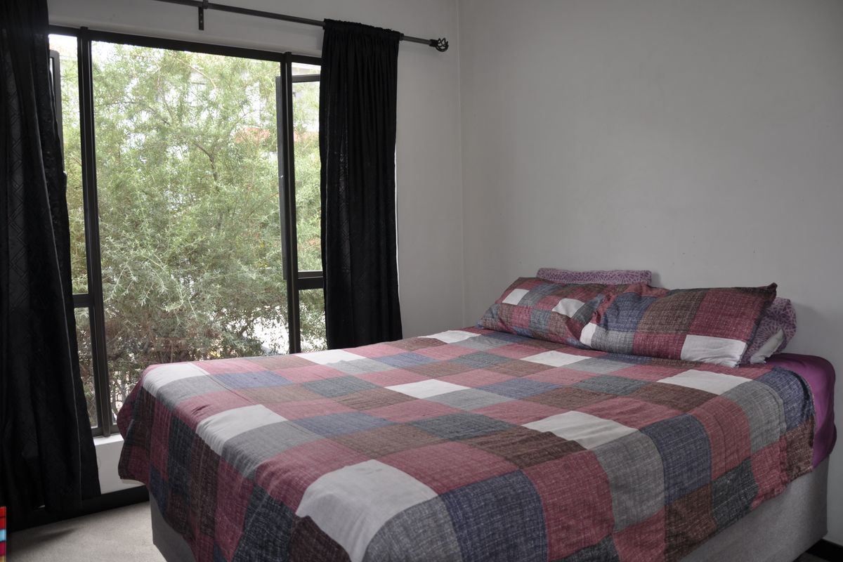 A bedroom featuring a large window with a curtain rod, providing natural light and a view of the surrounding greenery.