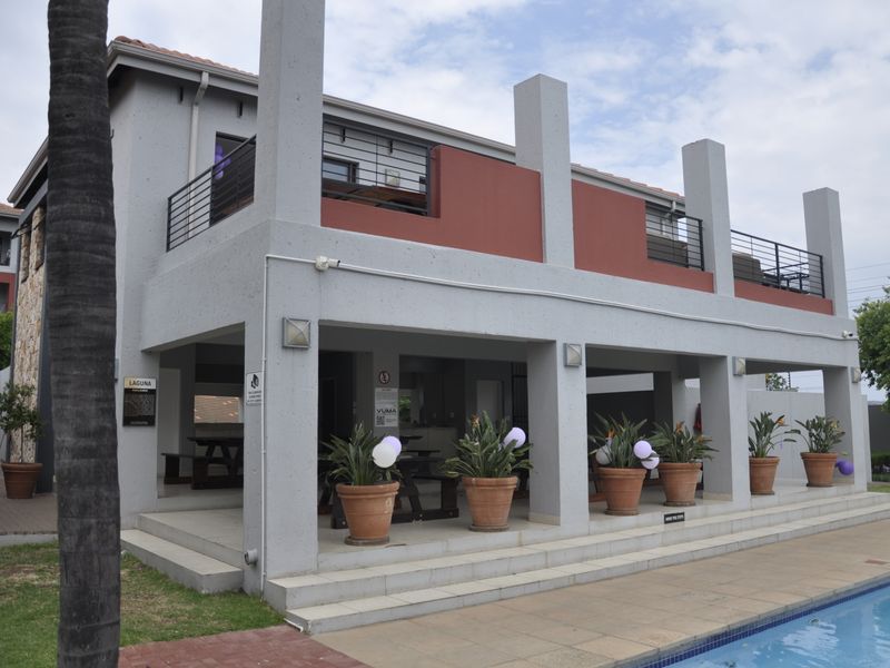 A well-maintained outdoor pool area featuring a covered patio with concrete pillars and an upper-level balcony with metal railings.
