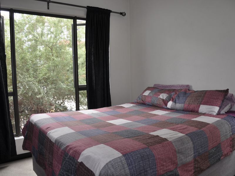 A bedroom featuring a large window with a curtain rod, providing natural light and a view of the surrounding greenery.