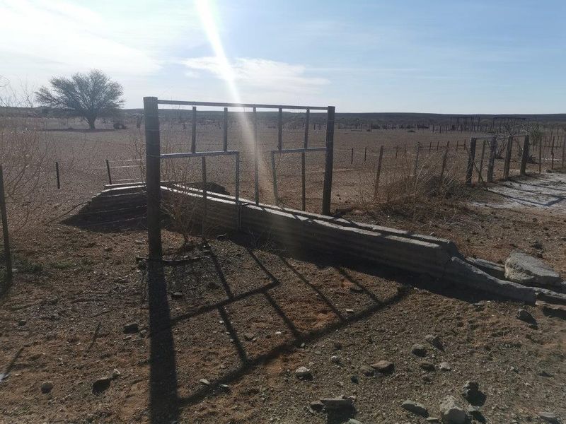 Outdoor farm area featuring a metal livestock fence and a concrete water trough in a dry, open landscape setting.