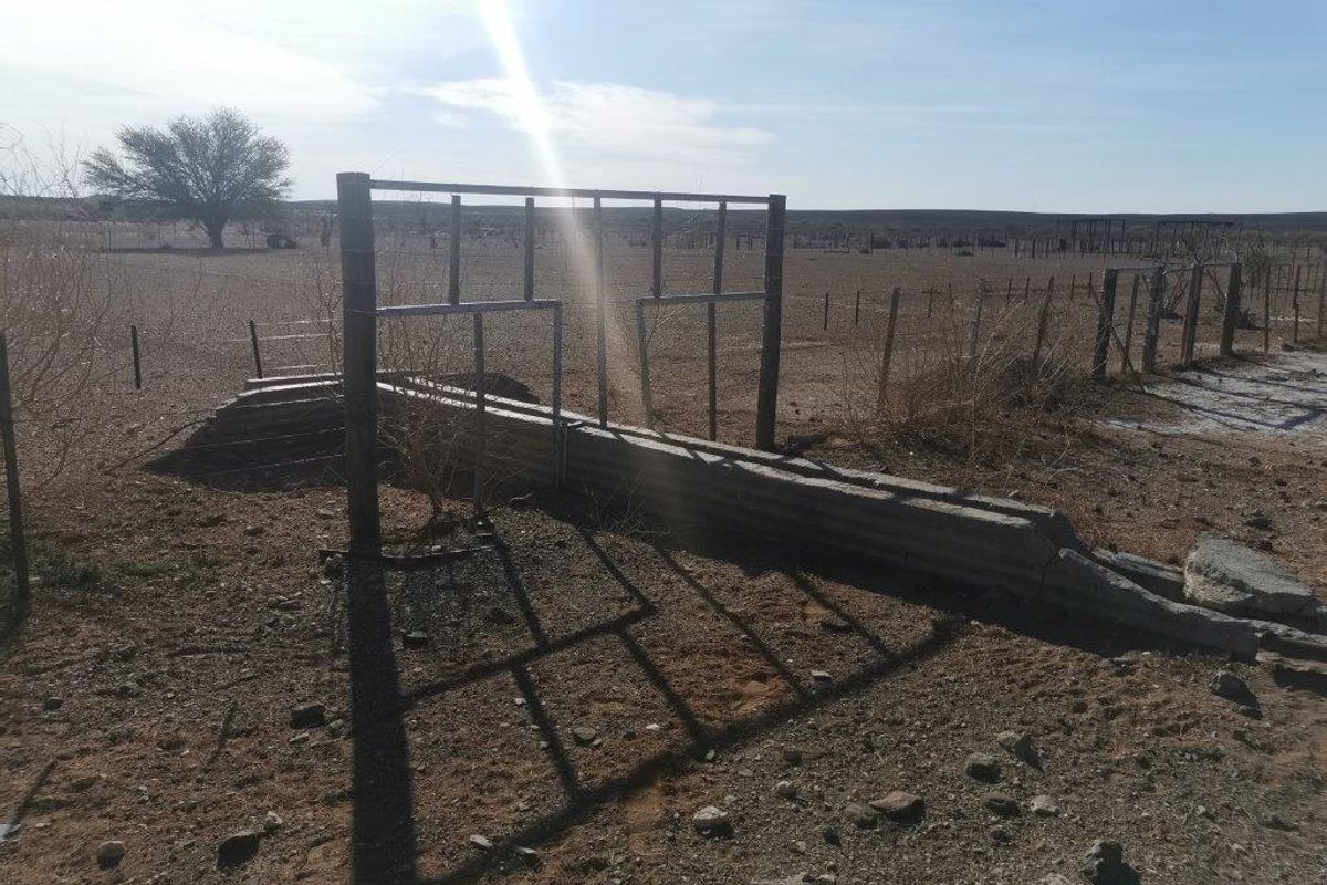Outdoor farm area featuring a metal livestock fence and a concrete water trough in a dry, open landscape setting.