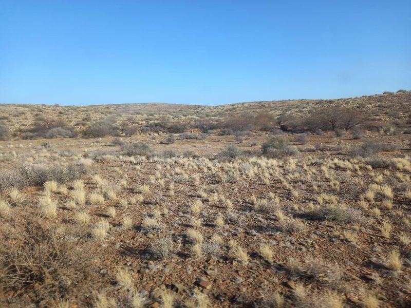 A wide-angle view of the expansive, arid farm landscape featuring natural scrub vegetation and rolling hills under a clear blue sky.