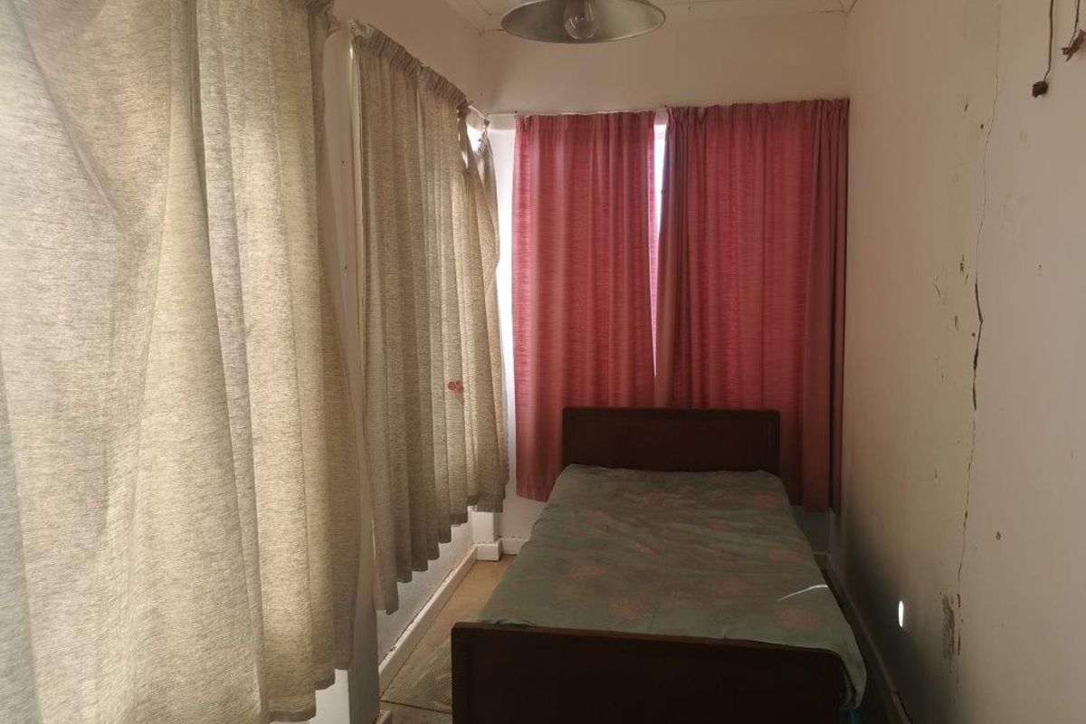 A bedroom featuring significant wall cracking and peeling paint, requiring structural repair and cosmetic renovation to restore the space.