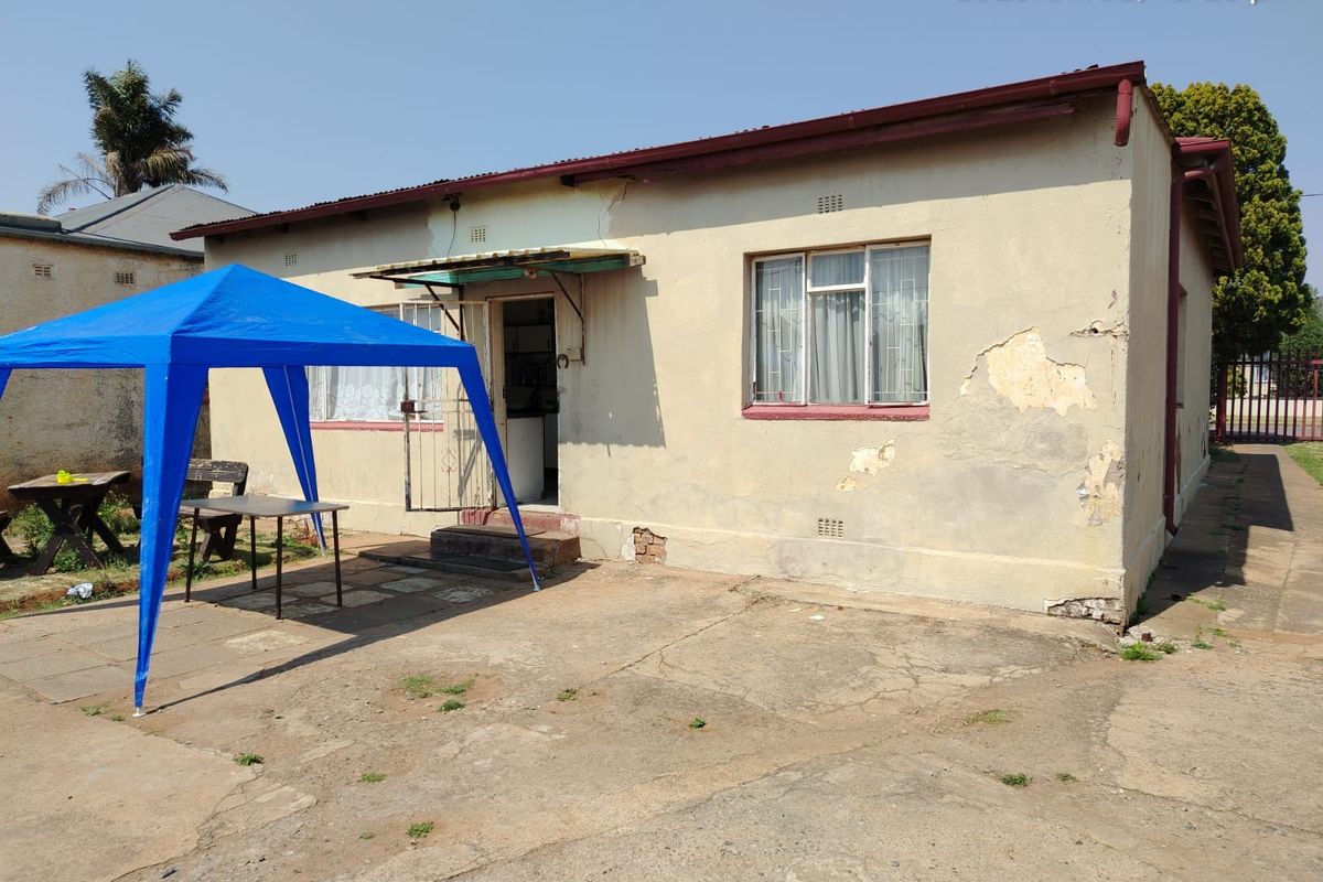 Rear exterior view of a house featuring a concrete patio area, showing significant wear to the exterior plaster and paintwork.