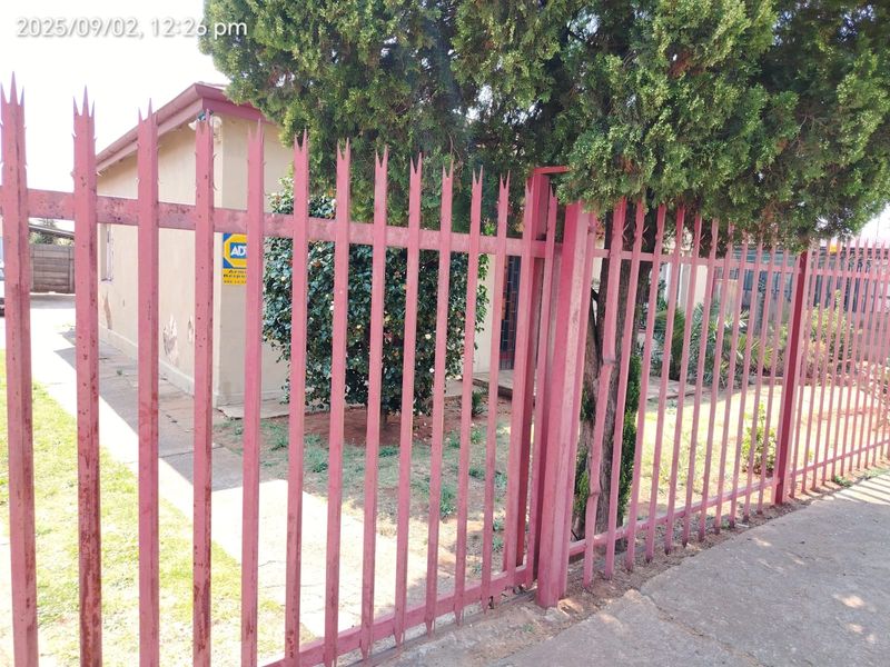 Front view of the property featuring a metal spike security fence and a paved walkway leading to the entrance.