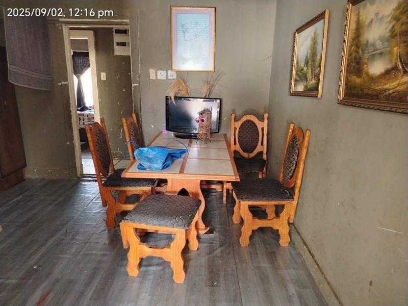 A dining area featuring laminate flooring and plain wall finishes, requiring cosmetic updates to improve the overall aesthetic and condition of the space.