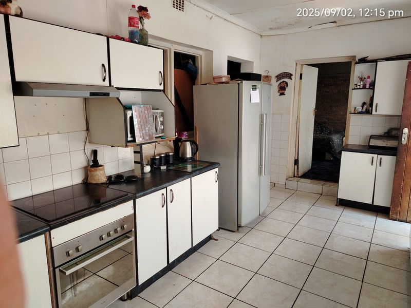 A functional kitchen featuring built-in cabinetry, an electric hob, oven, and tiled flooring, currently showing signs of wear and requiring cosmetic updates.
