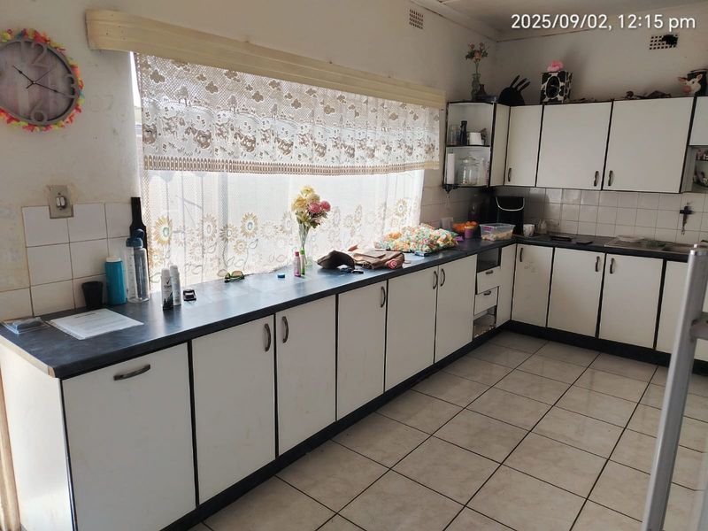 A dated kitchen featuring white cabinetry, dark laminate countertops, and ceramic floor tiles, offering a functional layout ready for modernization.