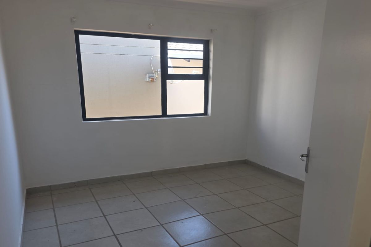 A clean, empty bedroom featuring neutral floor tiles and a large window with dark frames, providing a bright and versatile living space.