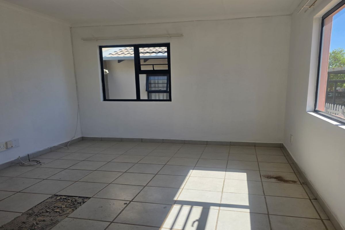 An empty living room featuring tiled flooring, large windows with black frames, and plain white walls, offering a blank canvas for interior design.