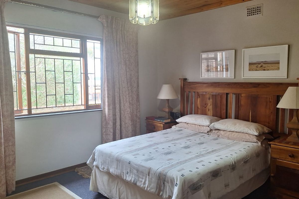 A bedroom featuring a timber-paneled ceiling, large window with security bars, and neutral wall finishes.