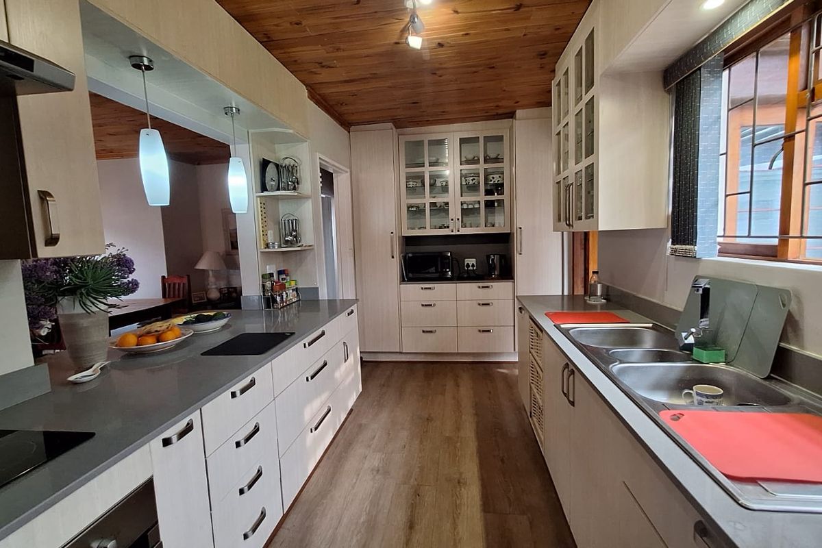 A well-maintained galley-style kitchen featuring light-toned cabinetry, stone-look countertops, double stainless steel sink, and a warm timber-paneled ceiling.