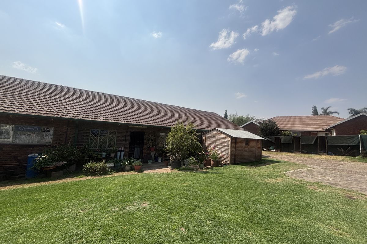 A view of the rear exterior of the house featuring a brick facade, tiled roof, a well-maintained lawn, and a detached wooden storage shed.