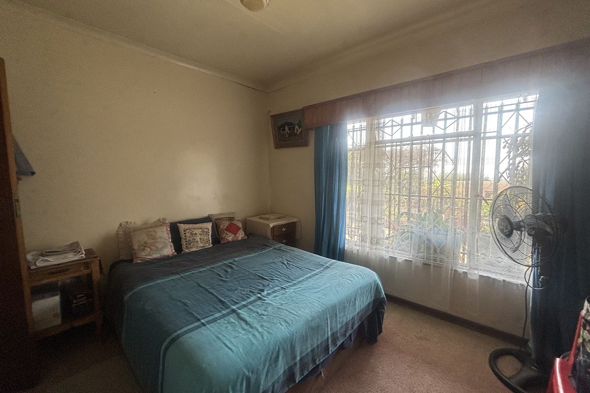 A bedroom featuring carpet flooring, a built-in wardrobe, and a window fitted with security bars.
