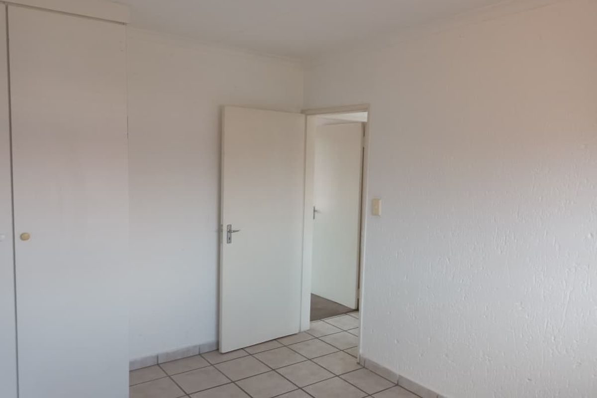 A simple, empty bedroom featuring built-in cupboards, tiled flooring, and neutral white walls, offering a blank canvas for personalization.