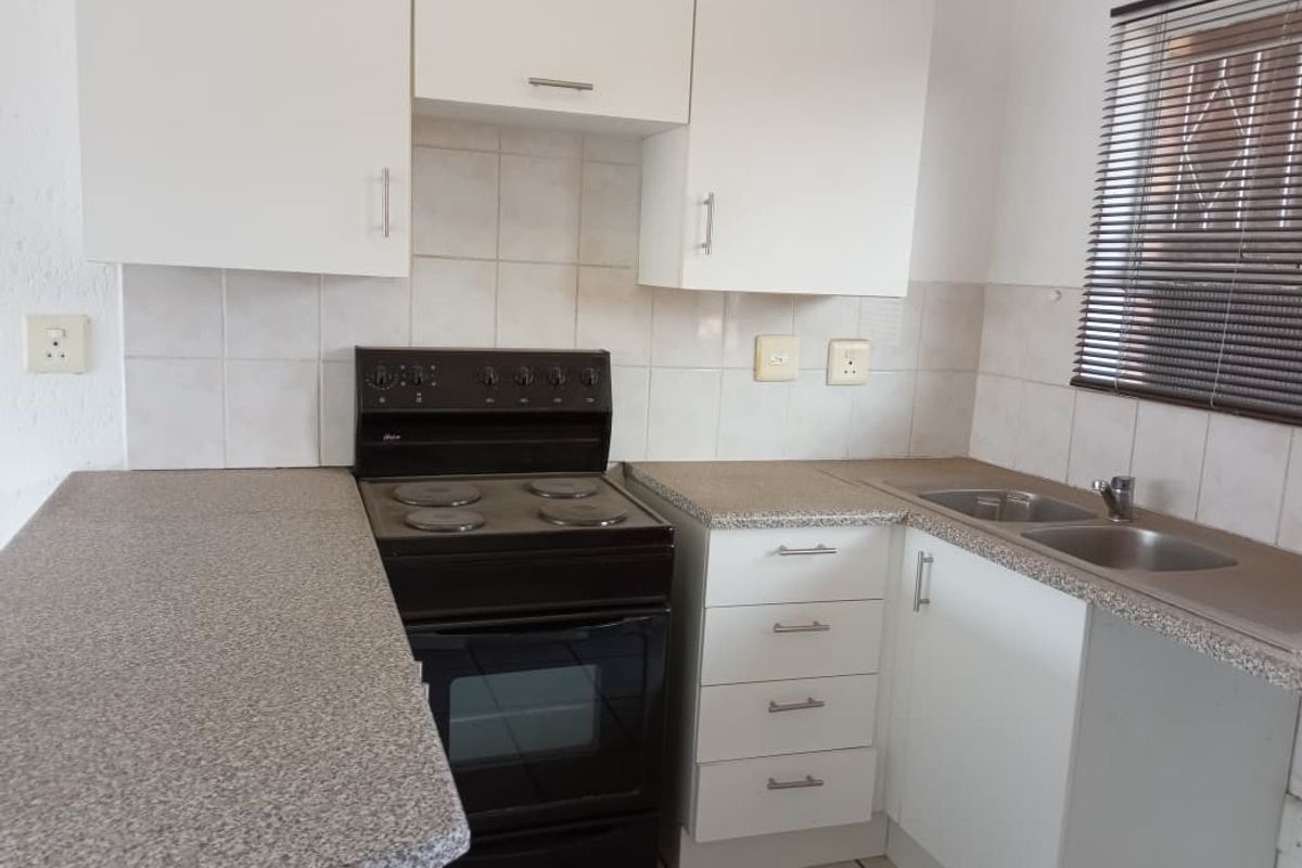 A functional kitchen featuring white cabinetry, a freestanding electric stove, granite-look laminate countertops, and a double stainless steel sink.