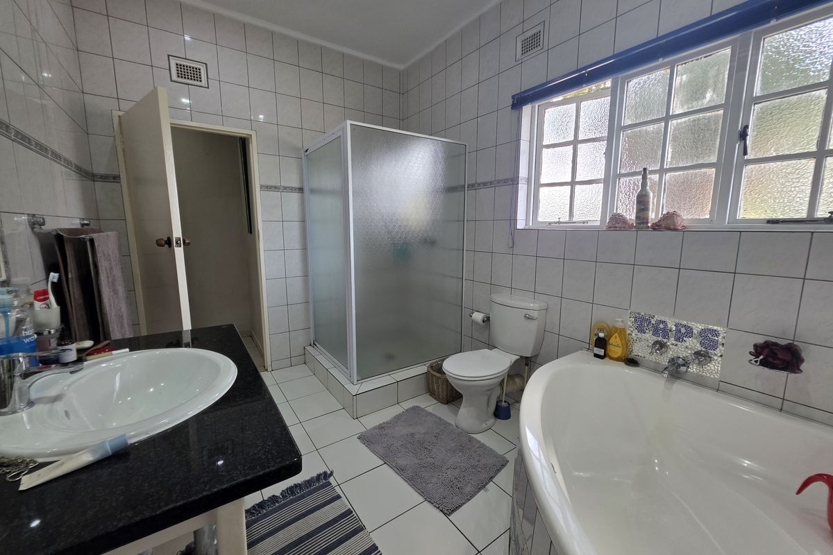 A functional bathroom featuring a shower enclosure, bathtub, toilet, and a vanity basin with a granite countertop, finished with full-height wall tiling.
