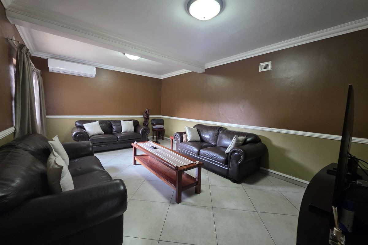 A spacious living room featuring ceramic tile flooring, crown molding, chair rail detailing, and a wall-mounted air conditioning unit.