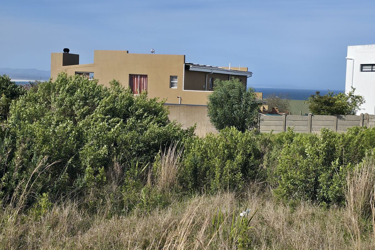 View of the rear elevation of a neighboring property from the vacant residential plot, featuring established coastal vegetation and boundary walling.