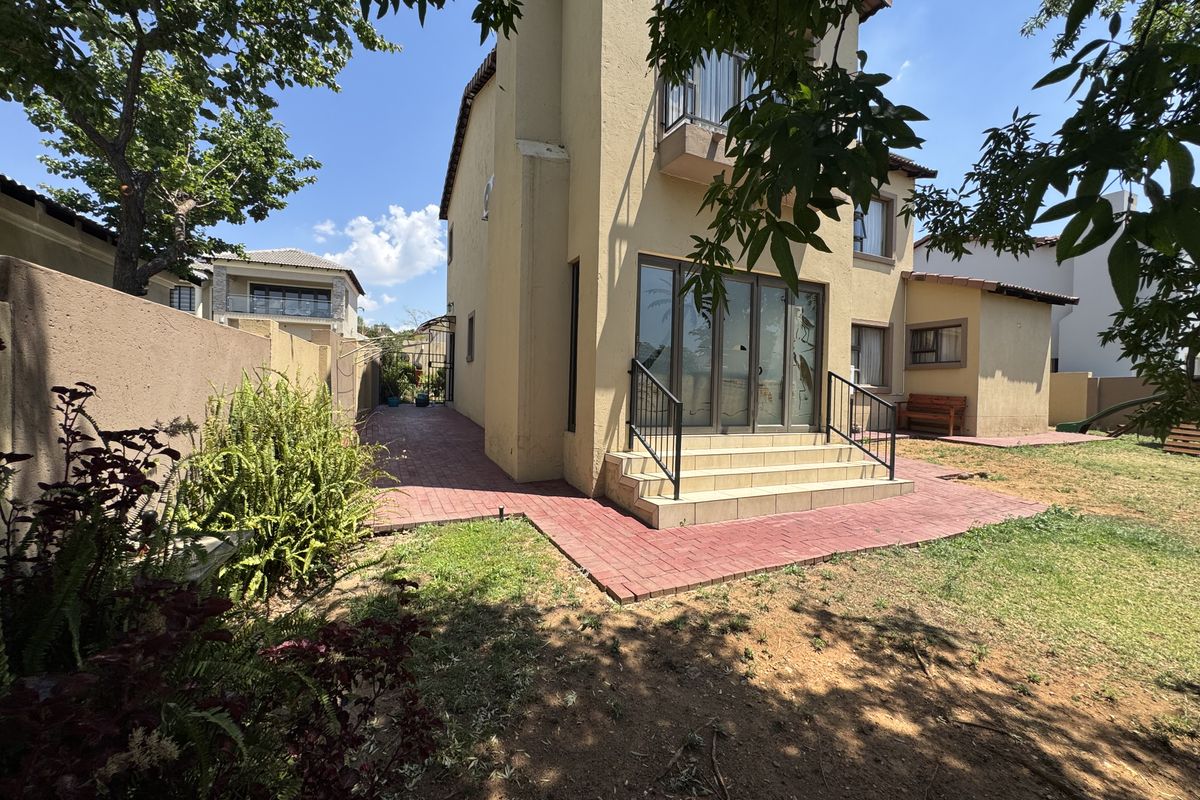 Rear view of the property featuring a paved patio area, steps leading to sliding glass doors, and a surrounding garden space.