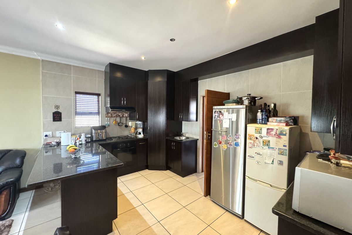 A functional kitchen featuring dark wood cabinetry, granite countertops, a breakfast bar, and tiled flooring with integrated cooking appliances.