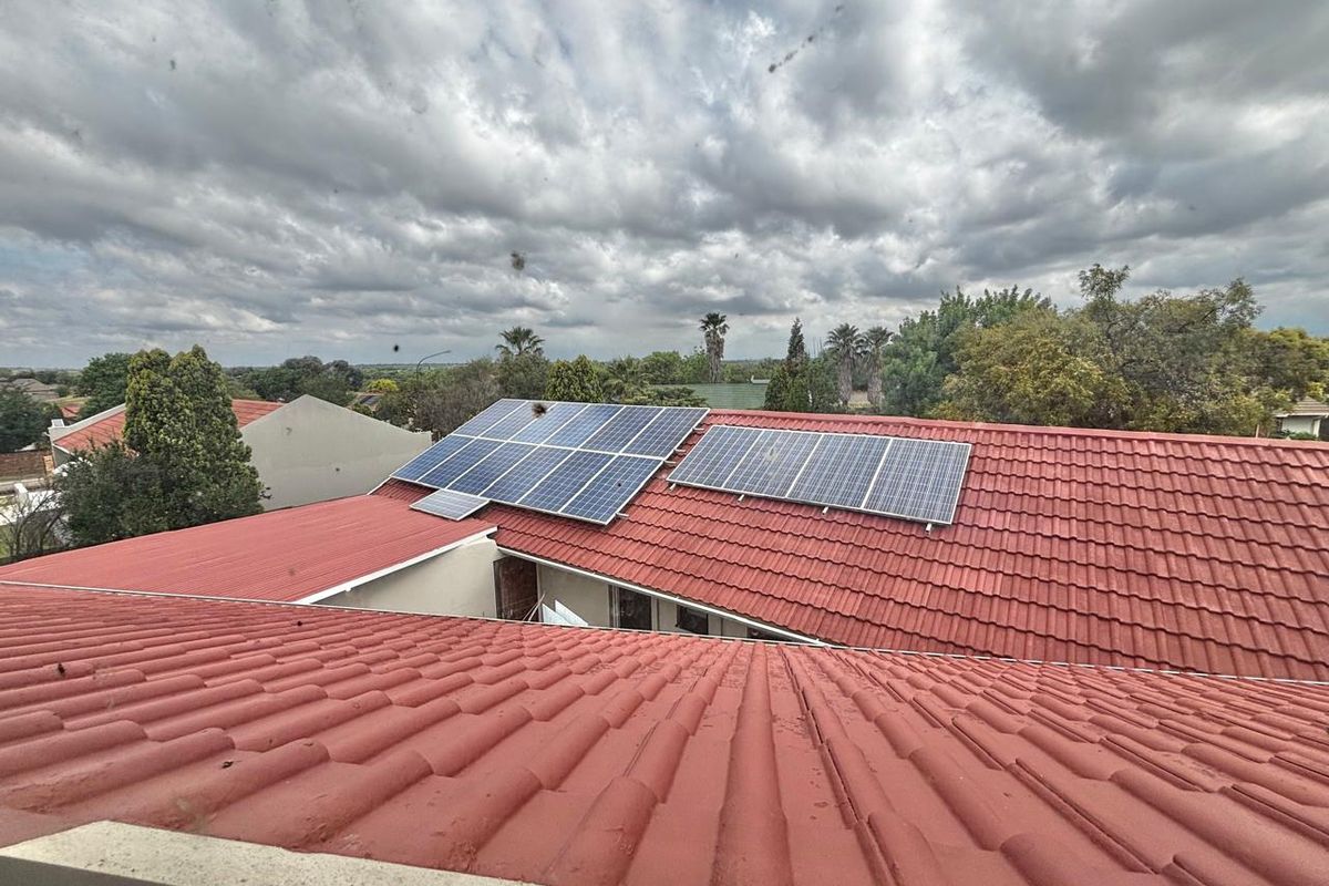 Elevated view of a red tiled roof featuring a mounted solar panel array, overlooking the surrounding residential neighborhood.