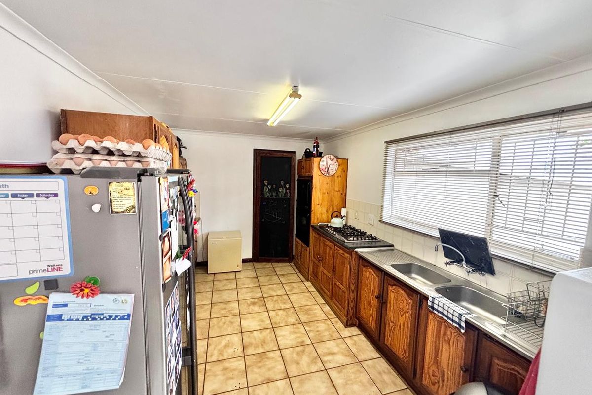 A functional kitchen featuring wooden cabinetry, a built-in gas hob, double stainless steel sink, and tiled flooring with ample natural light.