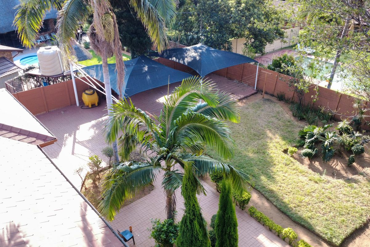 Aerial view of a spacious backyard featuring a paved patio area with shade sails, a landscaped garden, and perimeter boundary walls.
