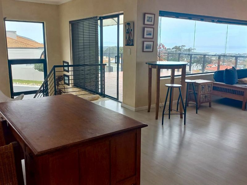 Spacious open-plan living area featuring large windows with scenic views, laminate flooring, and direct access to an outdoor balcony through sliding glass doors.