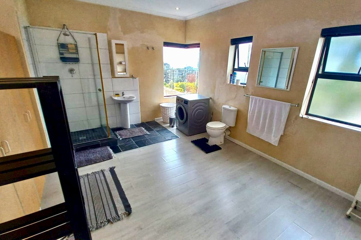 Spacious bathroom featuring a glass shower enclosure, pedestal sink, and toilet, with light-toned flooring and windows providing natural light.