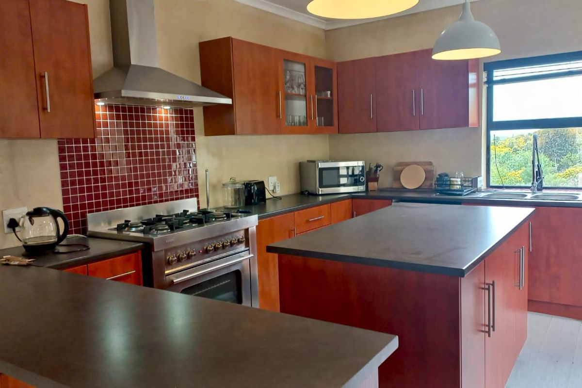 A functional kitchen featuring wooden cabinetry, a gas stove with extractor fan, a central island, and a tiled backsplash with a window view.